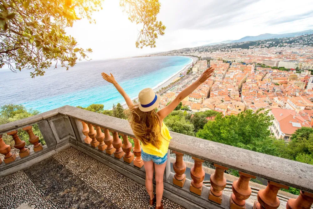 Woman with her arms raised on balcony overlooking Nice, France on a sunny day